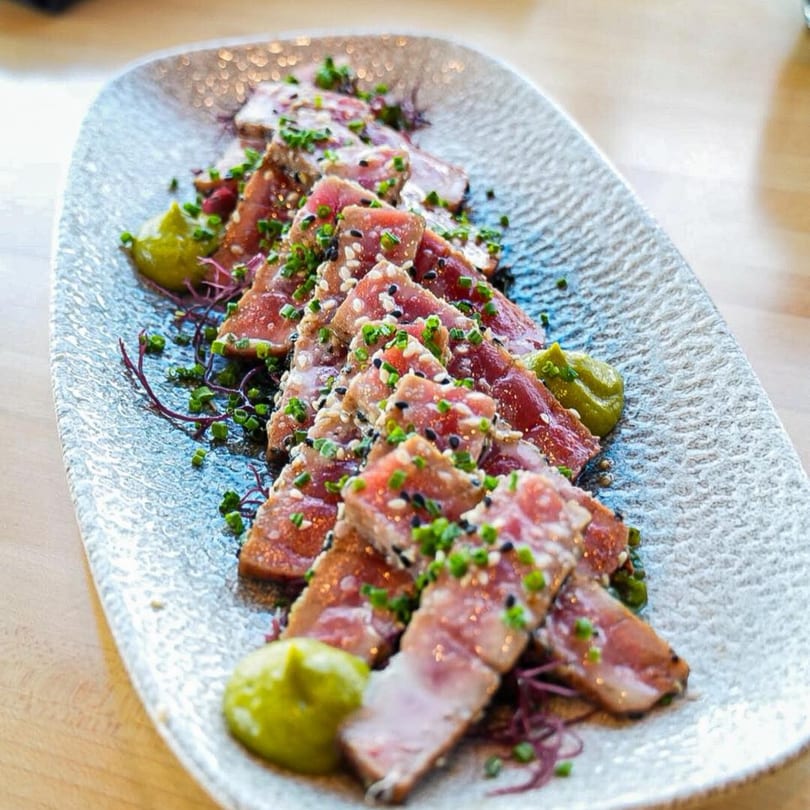 Seared tuna slices with sesame seeds, chives, and wasabi on a textured gray plate at SinDo PanAsian Cuisine.
