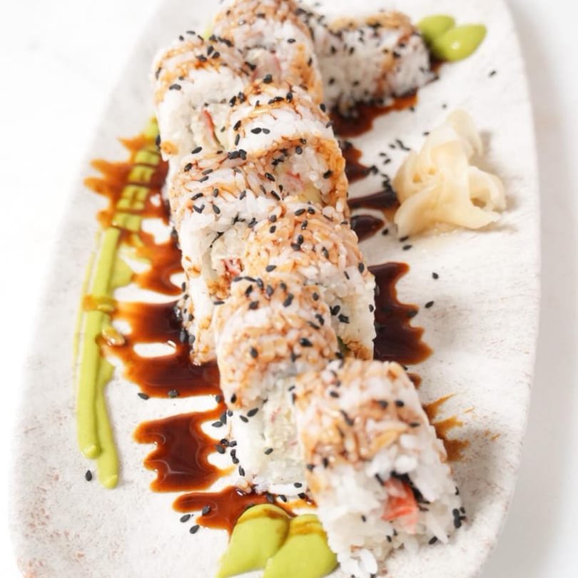 SinDo PanAsian Cuisine's sushi roll with black sesame seeds, drizzled with sauce, ginger, and wasabi.