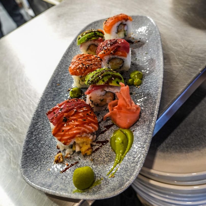 A long grey plate of SinDo PanAsian Cuisine sushi rolls topped with salmon, tuna, and avocado.